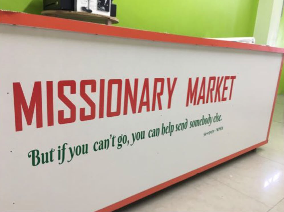 Missionary Market Shop signage counter reading 'But if you can't go, you can help send somebody else'
